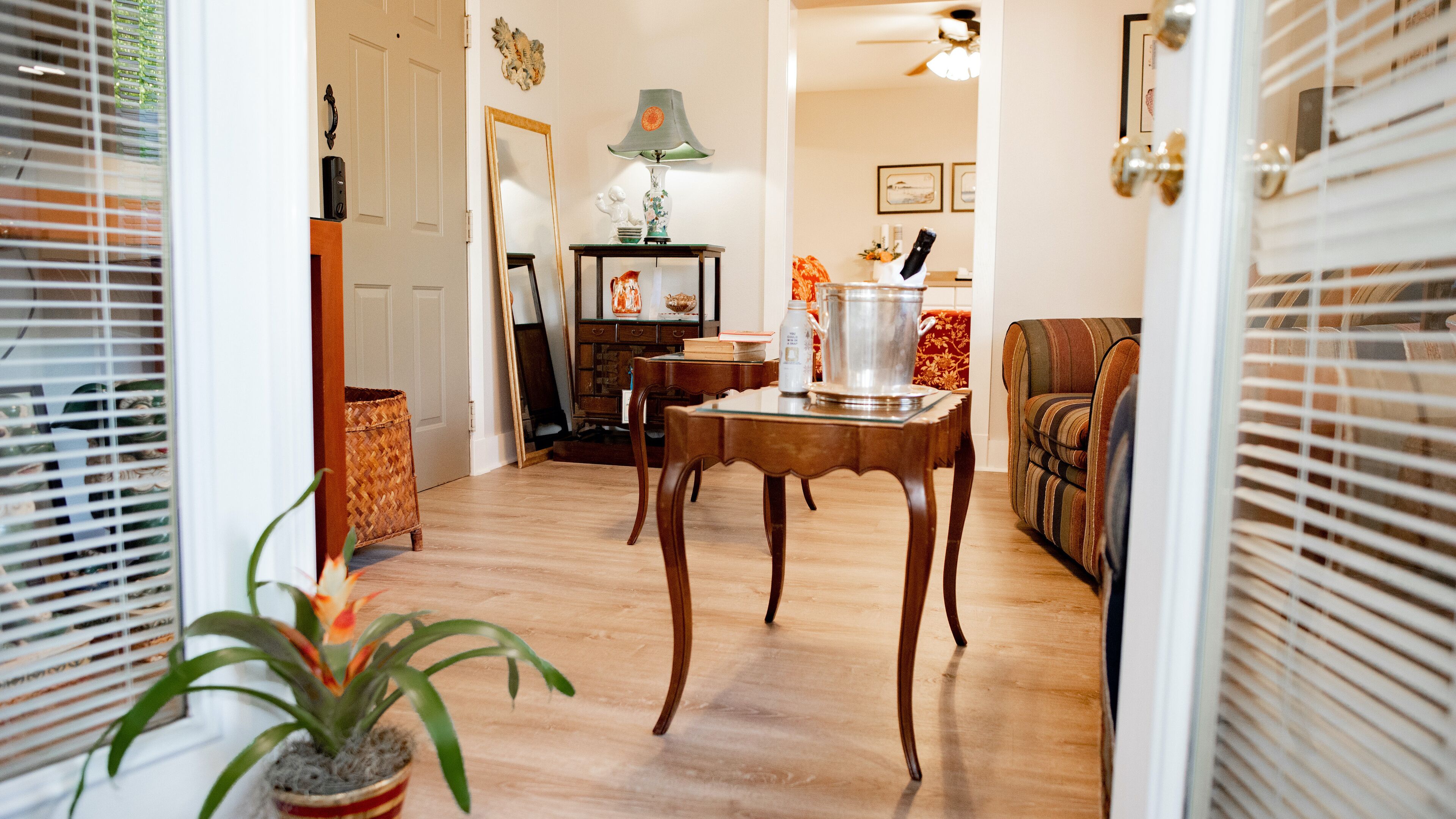 A hallway with wooden flooring, a dining table with chairs, a sofa, and a potted plant.
