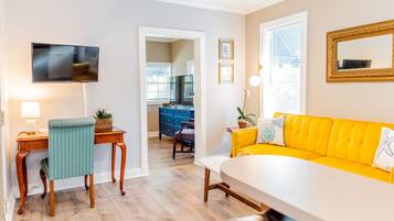 A modern living room with a yellow sofa, a wooden dining table, and a TV mounted on the wall.