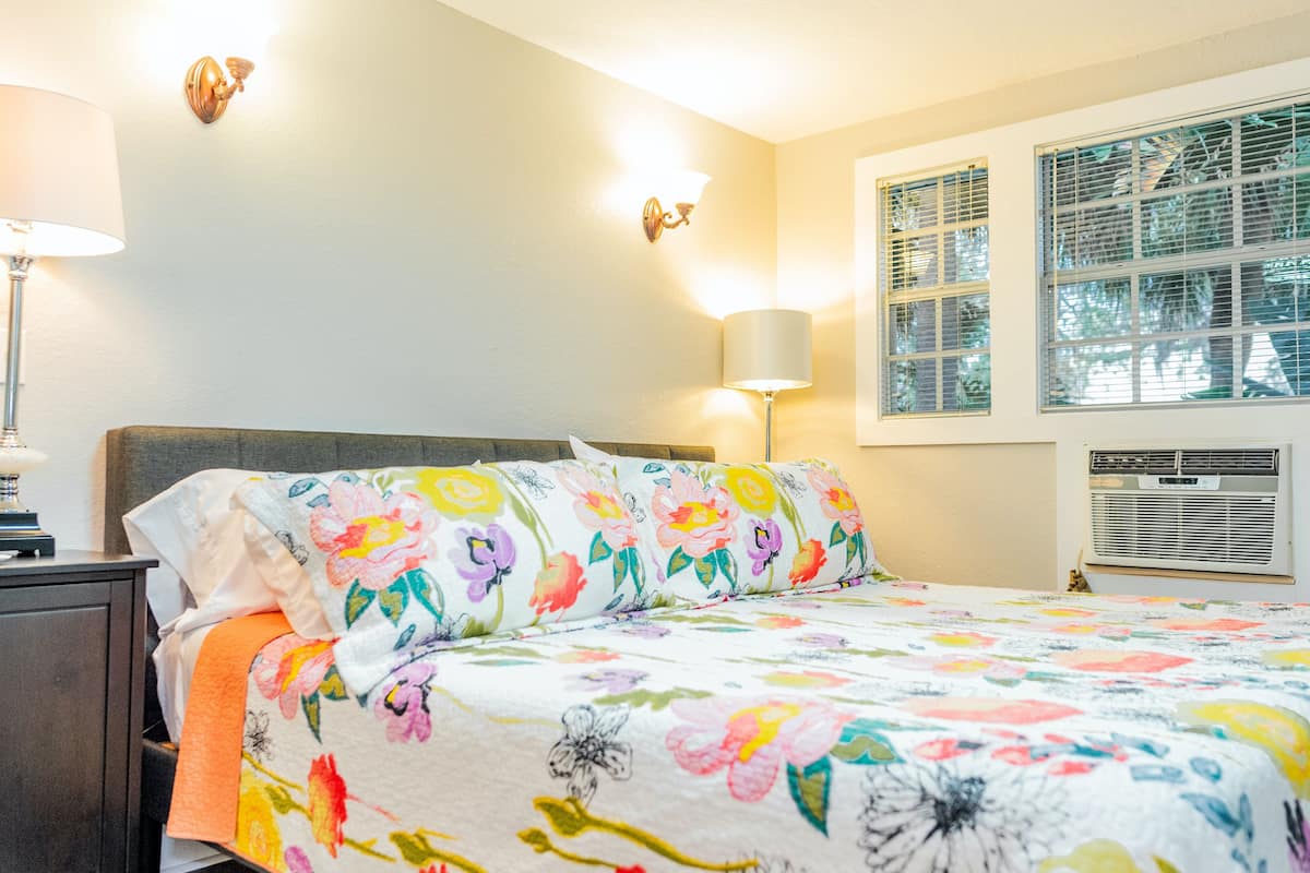 A bedroom with a bed, nightstand, two wall-mounted lamps, and a window with blinds.