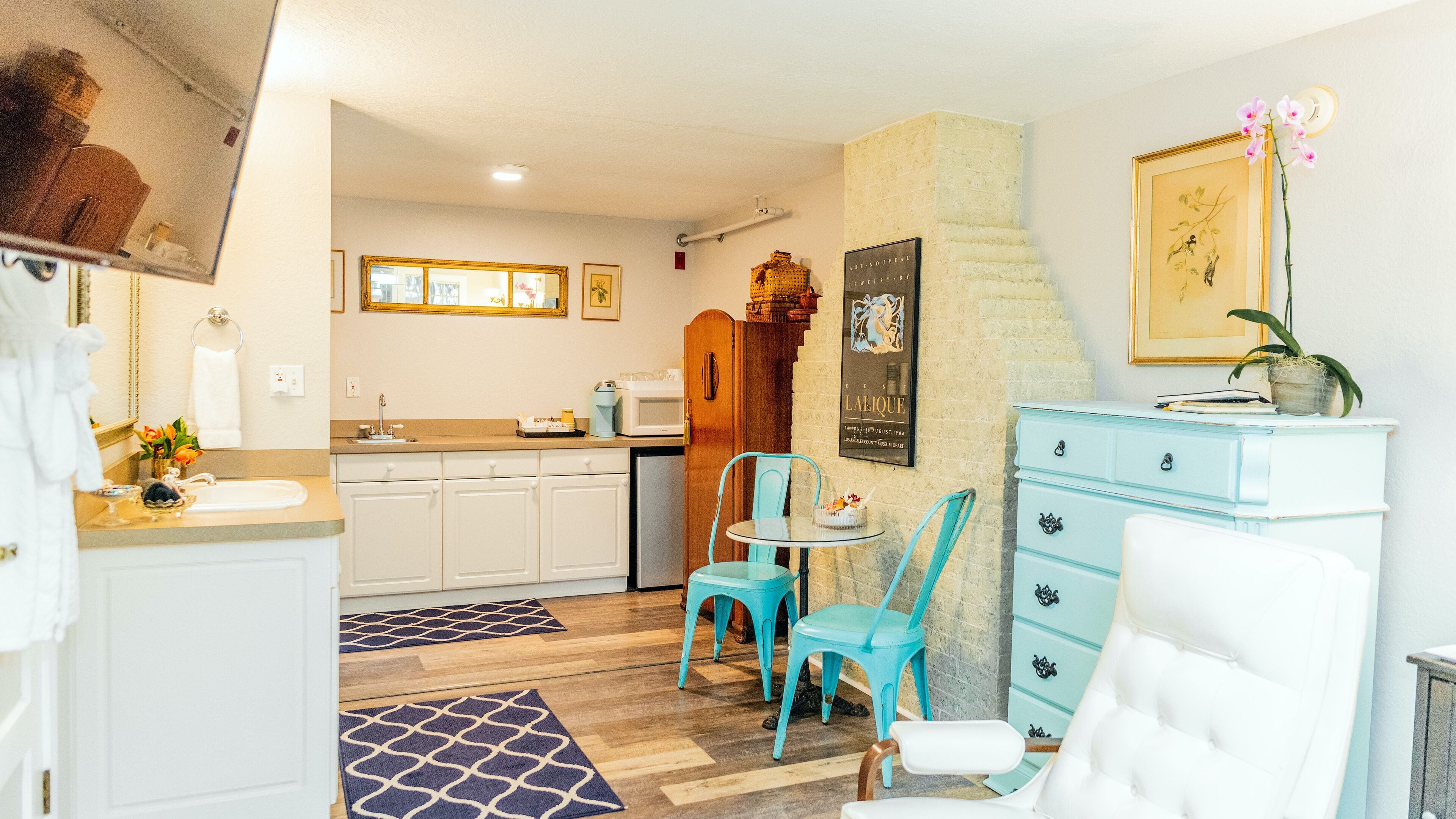 A compact kitchen with white cabinets, a wooden door, and a small dining area with turquoise chairs.