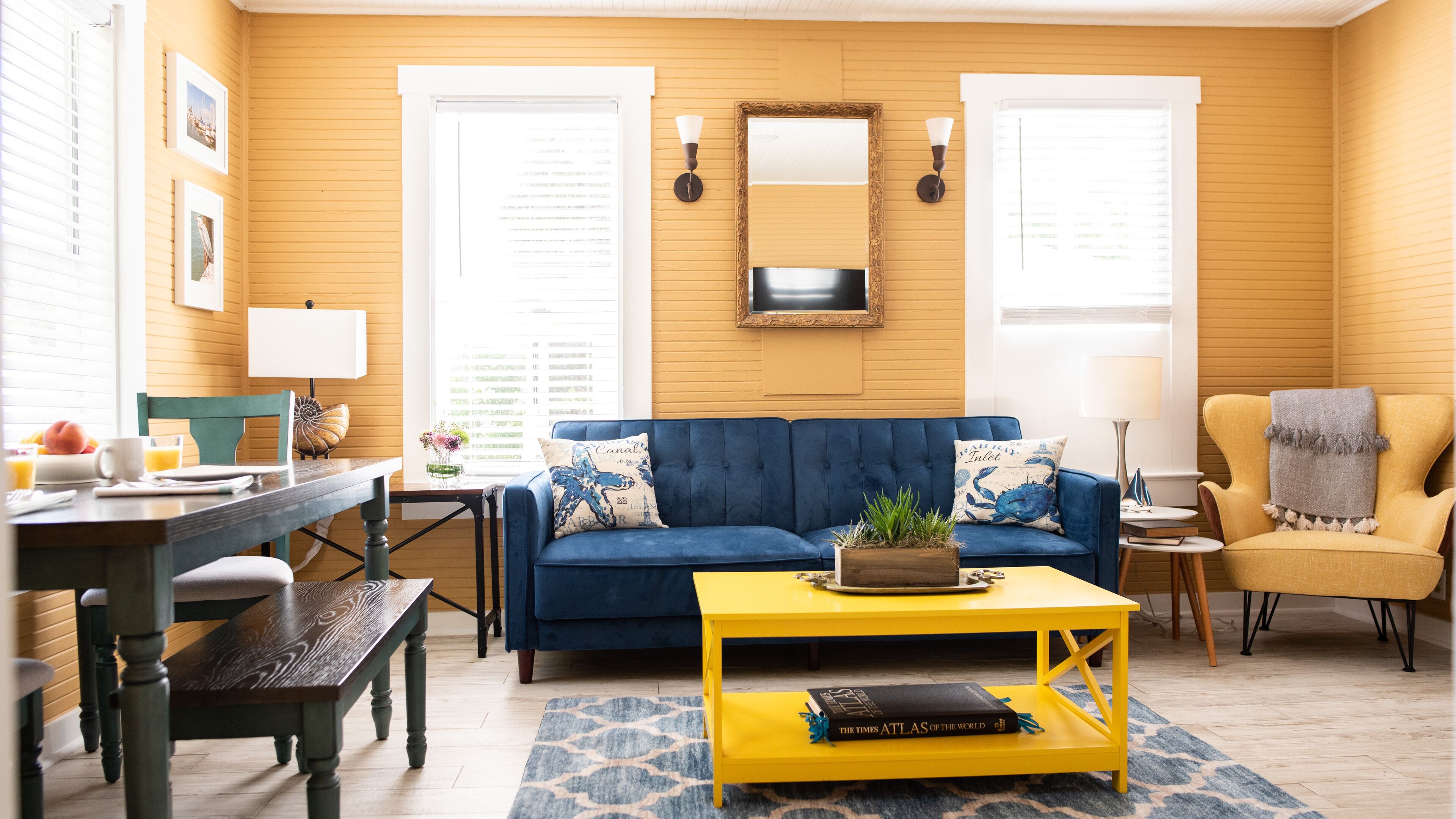 A living room with a blue sofa, yellow coffee table, and a wooden dining table.