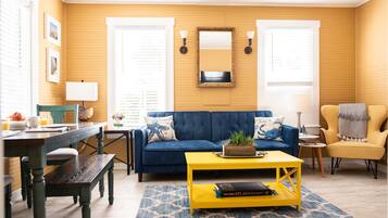 A living room with a blue sofa, yellow coffee table, and a wooden dining table.