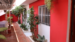 Un bâtiment rouge doté d’un espace extérieur abrité, de plantes en pot et d’une fenêtre grillagée.