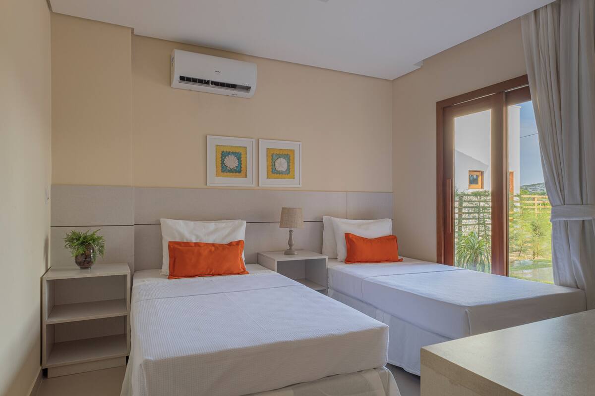 Habitación de hotel con dos camas, una mesita de noche, una lámpara y una planta en maceta.
