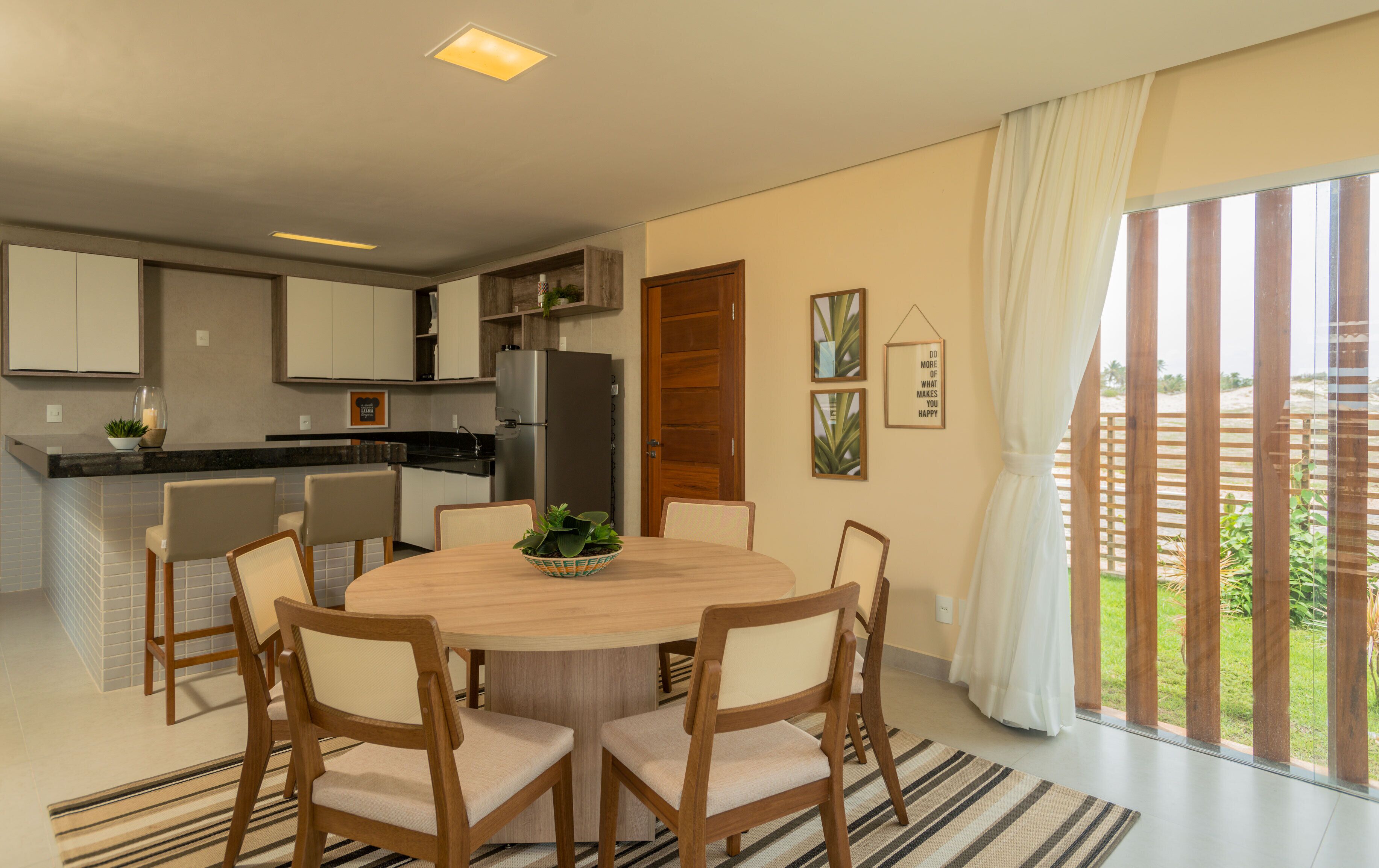 Cocina moderna con comedor, con una mesa redonda, sillas y vistas a un jardín a través de amplios ventanales.