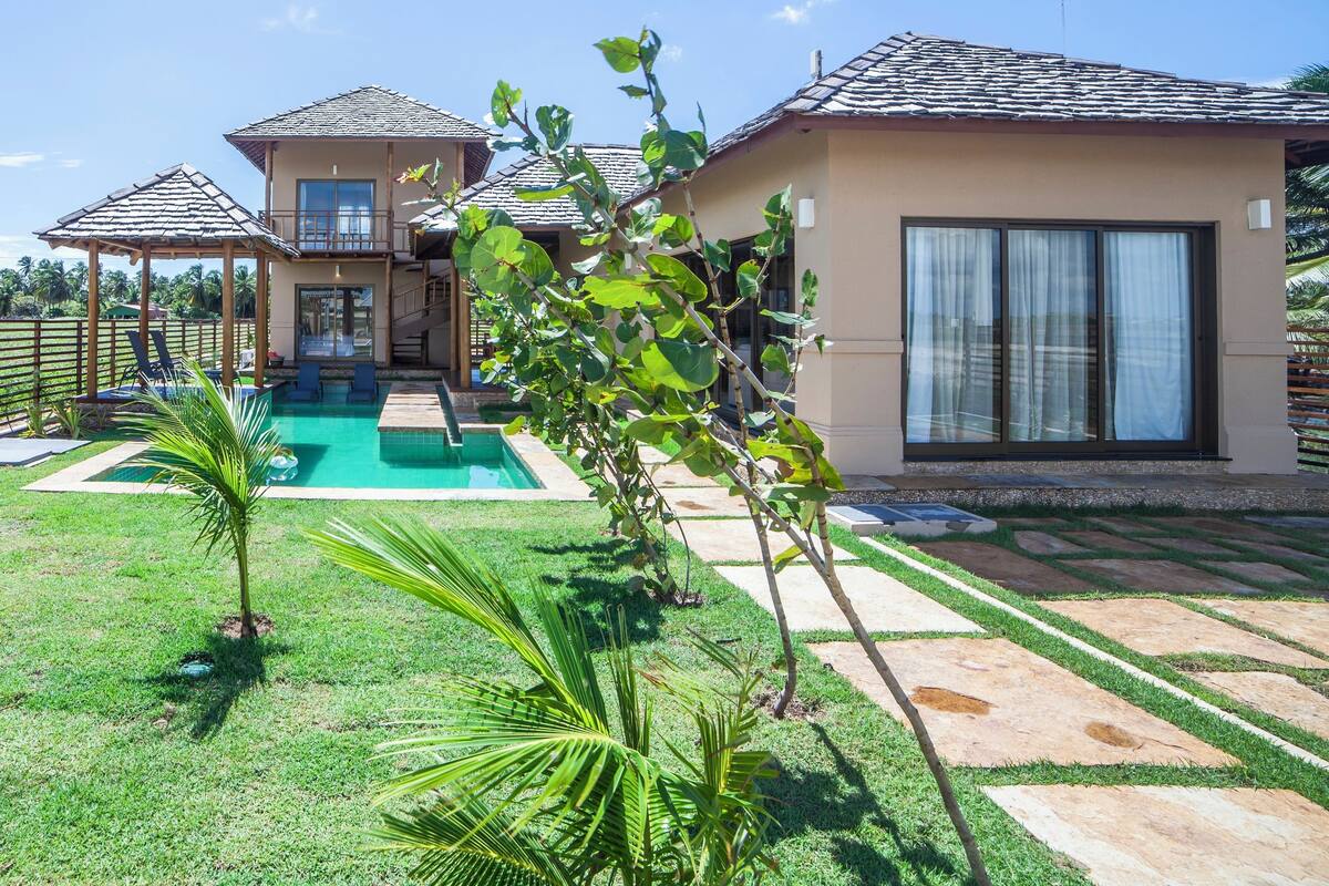 Una casa de dos pisos con piscina, un patio cubierto y un césped bien cuidado.