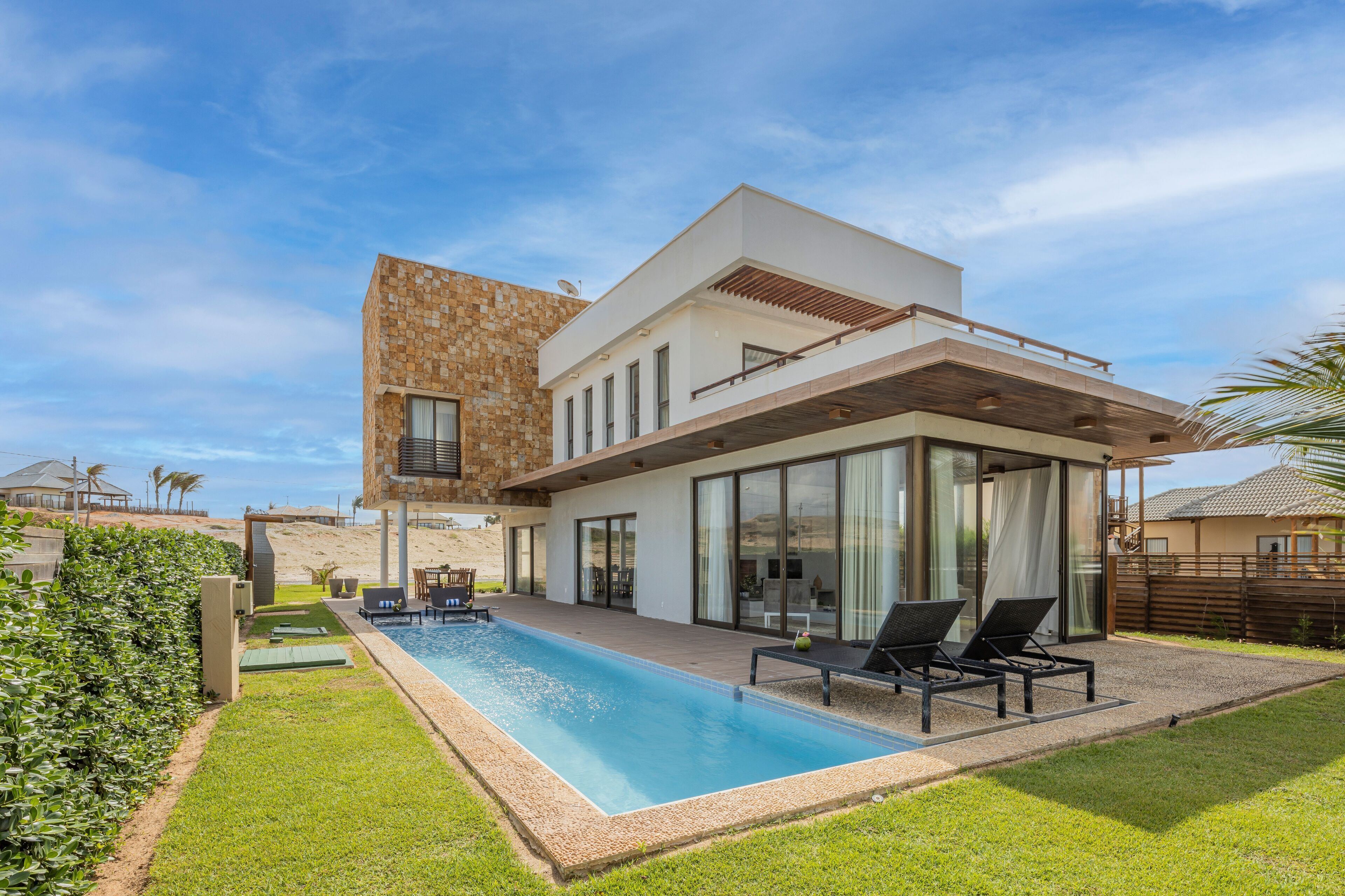 A modern two-story house with a swimming pool, outdoor seating, and a well-maintained lawn.