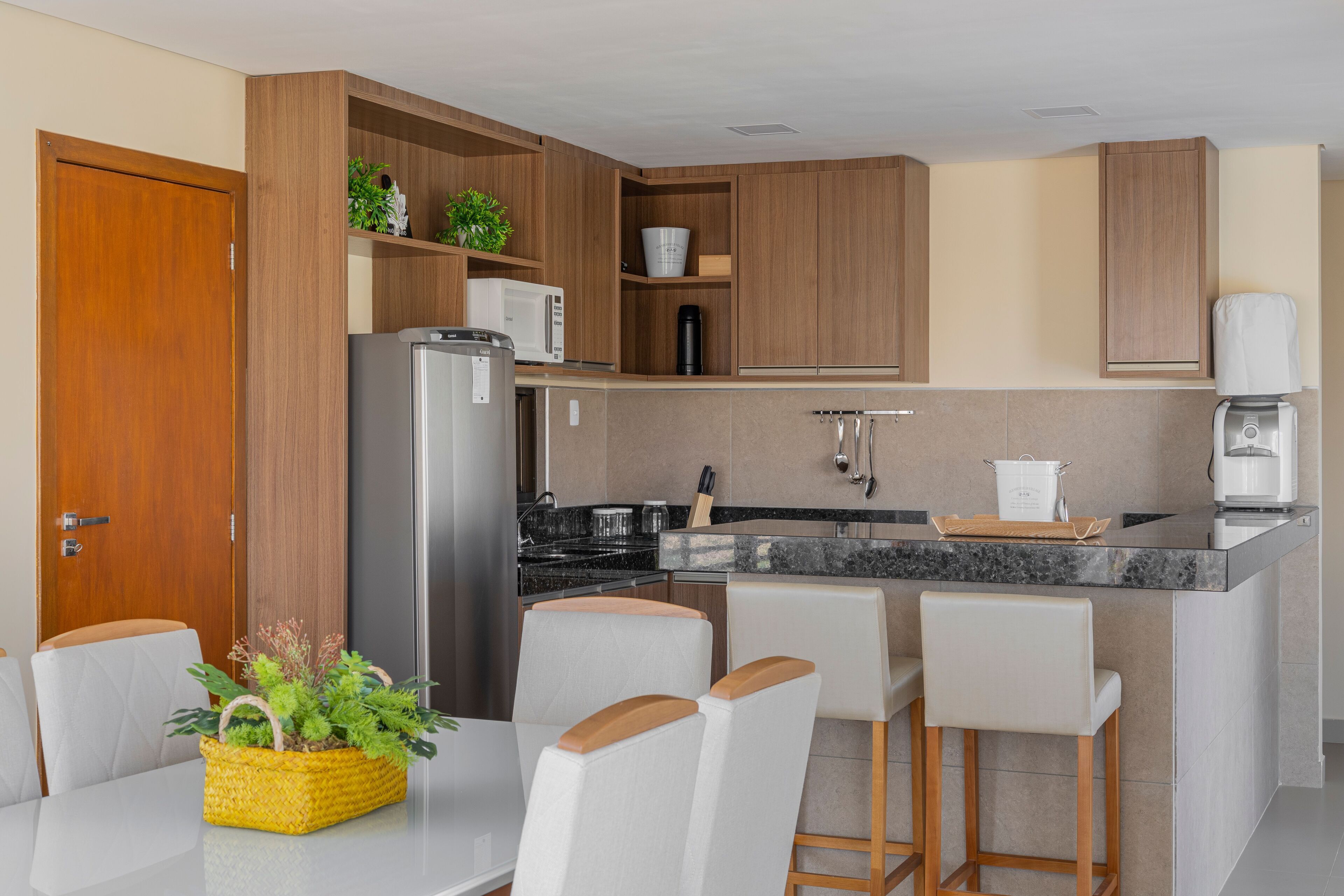 Une cuisine moderne avec des meubles en bois, un réfrigérateur, un four à micro-ondes, une machine à café et un coin bar avec des tabourets.