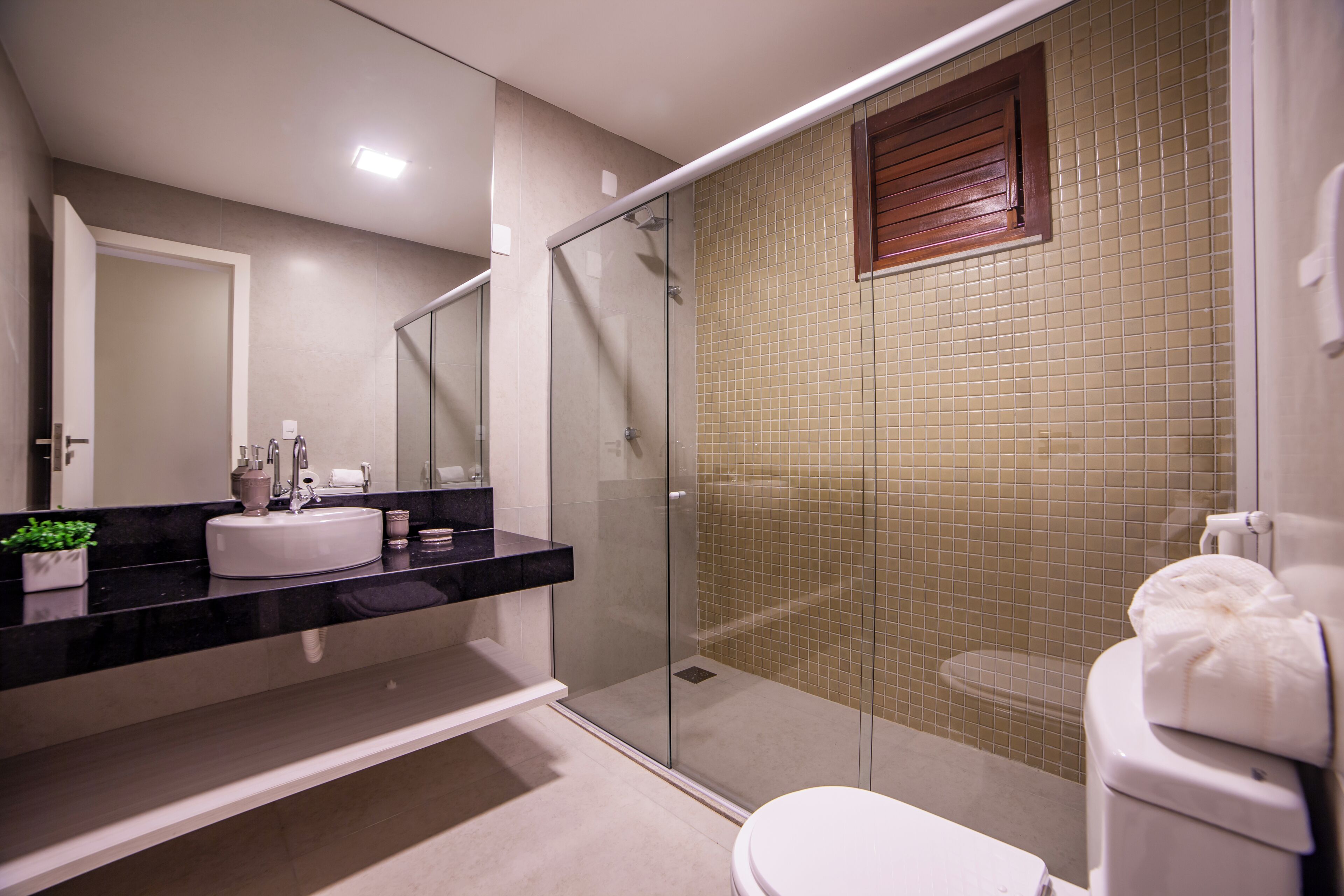 A modern bathroom with a glass-enclosed shower, a white toilet, and a black countertop with a sink and mirror.