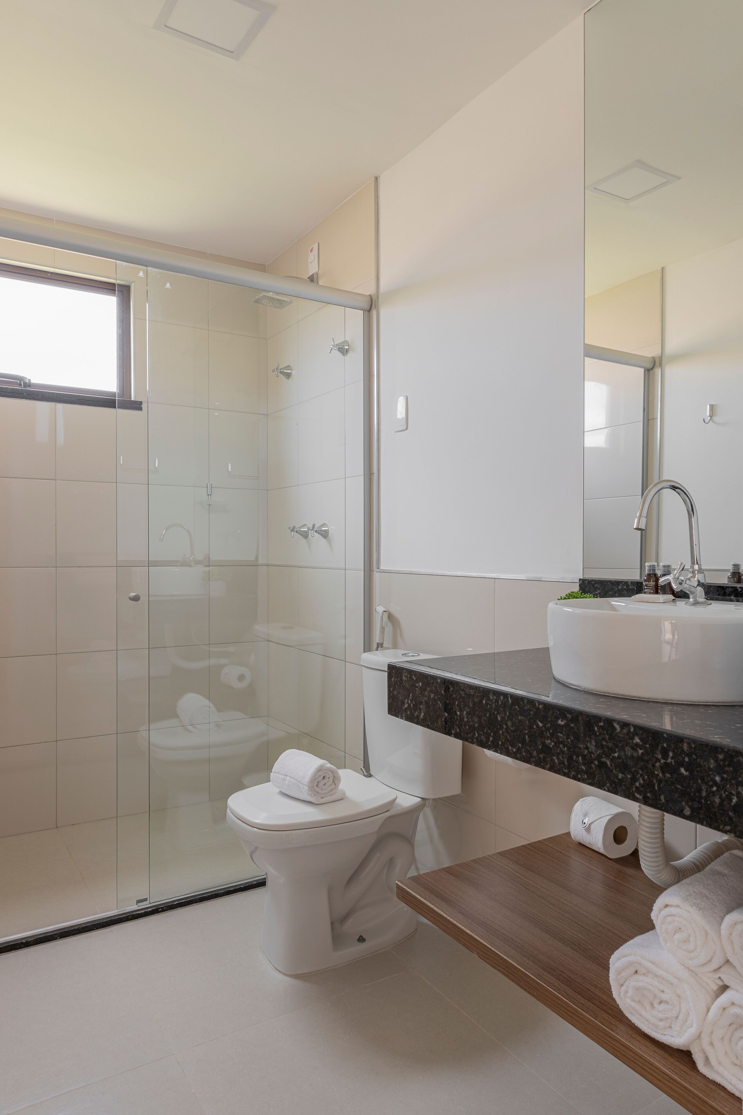 Un baño moderno con ducha de vidrio, inodoro blanco, lavamanos con encimera de mármol y espejo sobre el lavamanos.