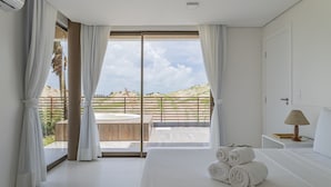 Ein Hotelzimmer mit einem großen Bett, Blick ins Freie und einem kleinen Tisch mit einer Lampe.