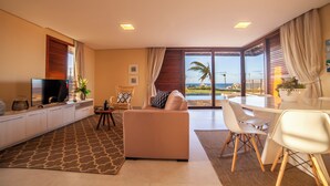Ein modernes Wohnzimmer mit einer Couch, einem Esstisch, Stühlen, einem Fernseher und Blick auf den Ozean.