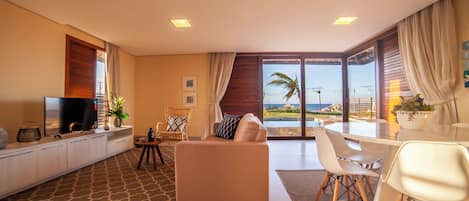 A modern living room with a sofa, dining table, and chairs, a TV, and a view of the ocean.