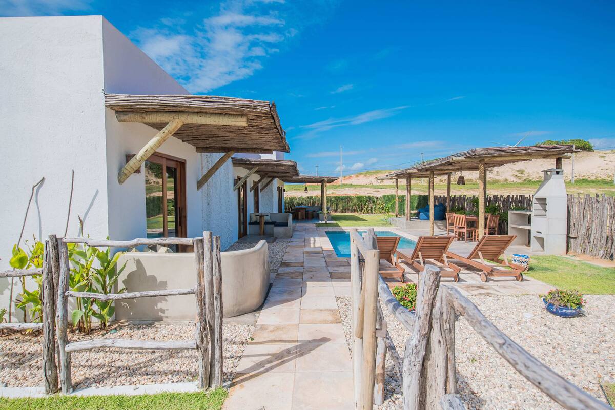 Un patio exterior moderno con piscina, mobiliario de madera y un edificio blanco.