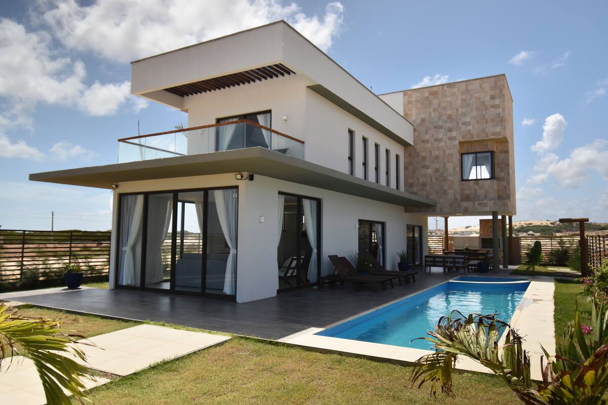 Una casa moderna de dos pisos con piscina, puertas de vidrio amplias y un balcón.