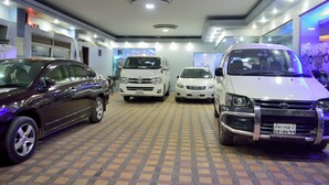 Salão de exposição com quatro carros, piso ladrilhado e teto com iluminação embutida.