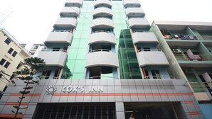 Um hotel com vários andares, design moderno, com varandas em cada andar e sinalização chamativa para "Cox's Inn".