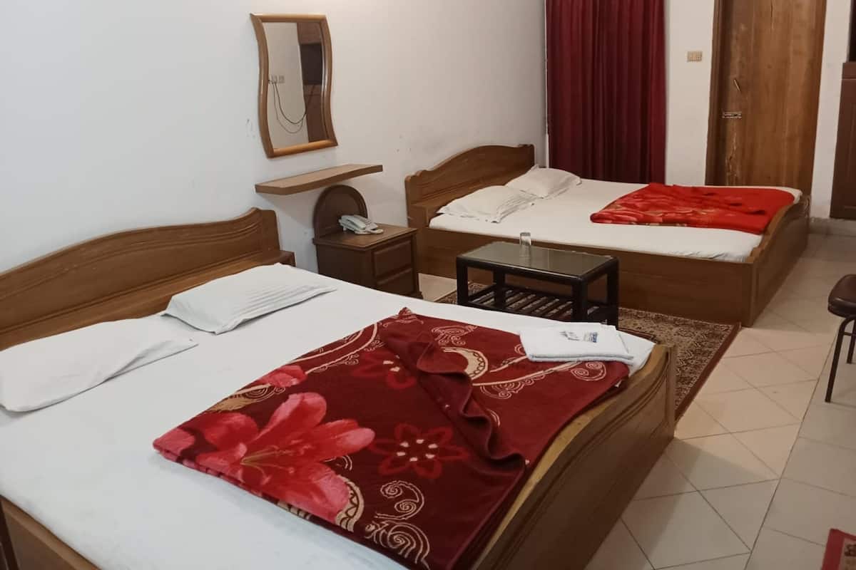 A hotel room with two wooden beds, a small table, a nightstand, a mirror, and a red curtain.