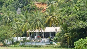 A bungalow with a tiled roof, surrounded by palm trees and a grassy field. - Siyambala Villa (Unawatuna)