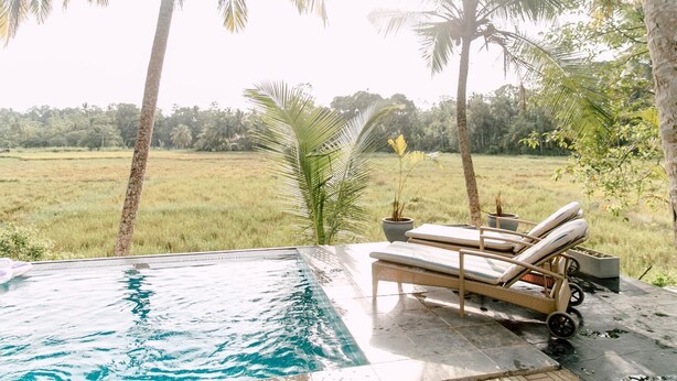 An infinity pool with lounge chairs, surrounded by palm trees and a view of a grassy field. - Siyambala Villa (Unawatuna)