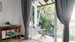A room with a wooden chair and table, a balcony with a railing, and a view of greenery outside. - Siyambala Villa (Unawatuna)