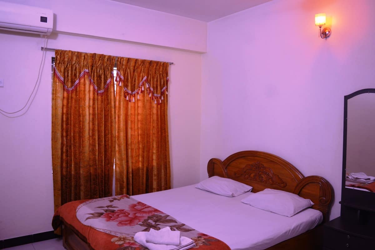 A hotel room with a bed, a wooden headboard, a nightstand, a mirror, and a window with curtains.