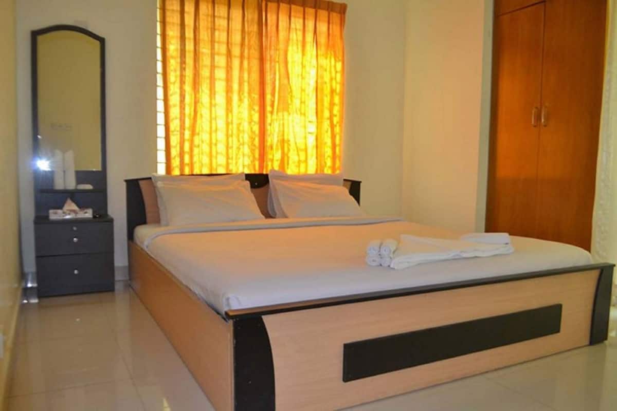 A neatly made bed with white linens, a bedside table with a lamp, and a large mirror on the wall.