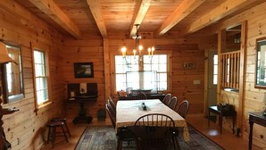 A wooden cabin with a dining area featuring a long table and chairs, a chandelier, and a view of a lake.