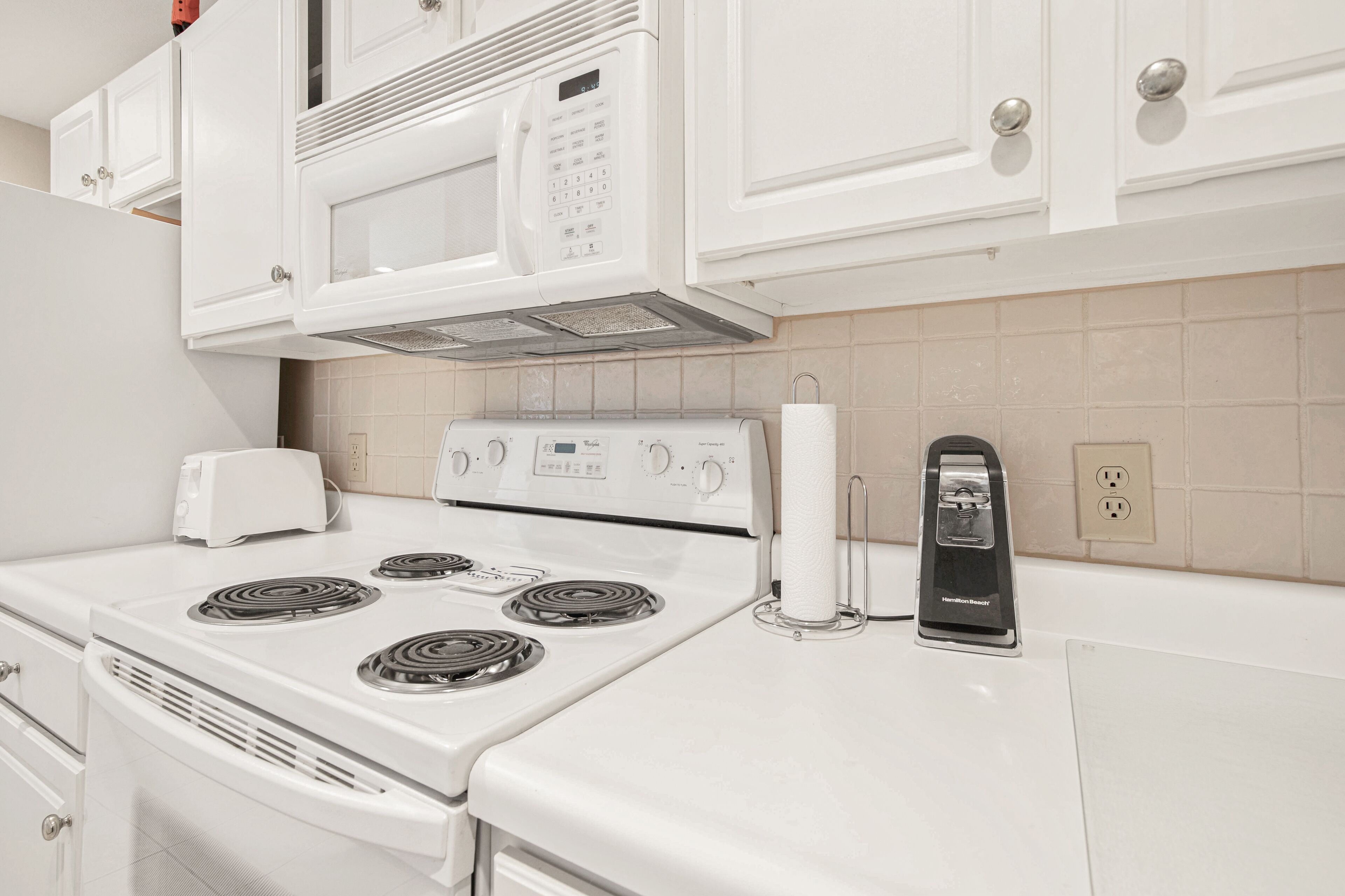 Une cuisine avec des appareils électroménagers blancs, notamment une cuisinière, un four à micro-ondes et un grille-pain.