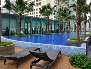 Una piscina moderna al aire libre con borde de azulejos, rodeada de palmeras y sillones de descanso.