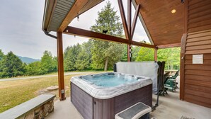 Un jacuzzi en un espacio exterior cubierto con un banco de piedra y vistas al bosque.