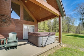 Una cabaña de madera con un porche cubierto, un jacuzzi, una silla Adirondack verde y un ventanal grande.