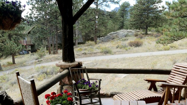 Een houten terras met schommelstoelen en een tafel, met uitzicht op een natuurlandschap met bomen en een weg.