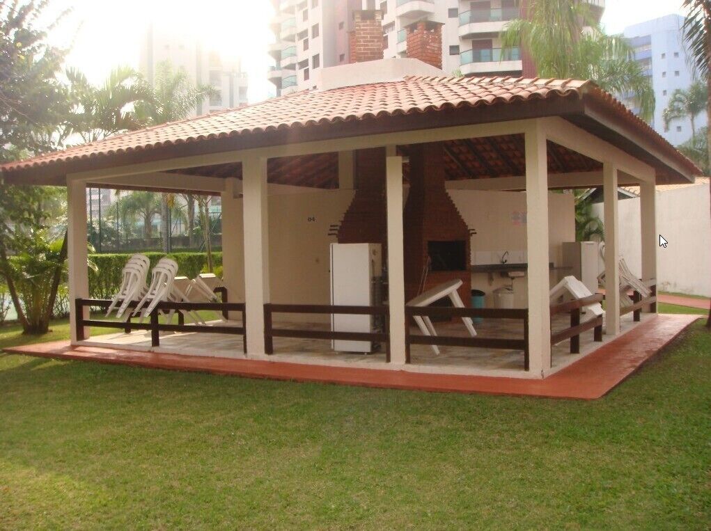 A covered outdoor seating area with chairs and a table, surrounded by a low brick wall and a small garden.