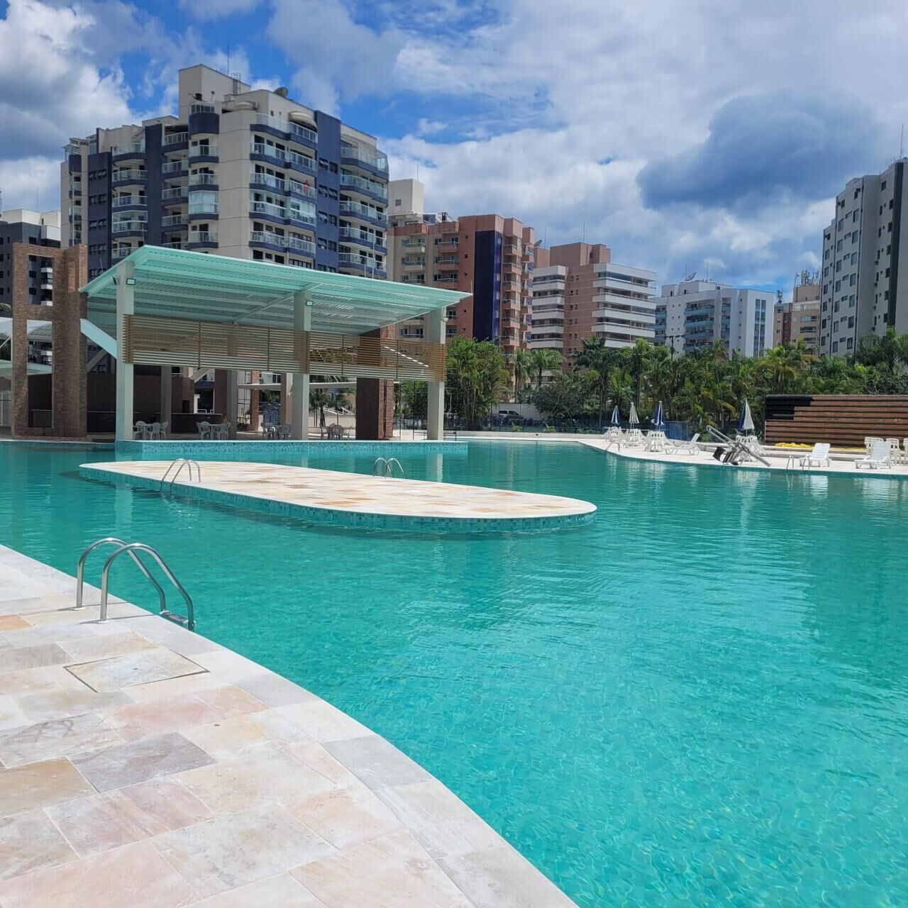 A swimming pool with a covered seating area, surrounded by high-rise buildings.