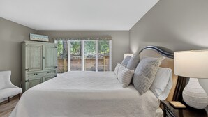 A bedroom with a bed, a nightstand, a lamp, a wardrobe, and a window with blinds.