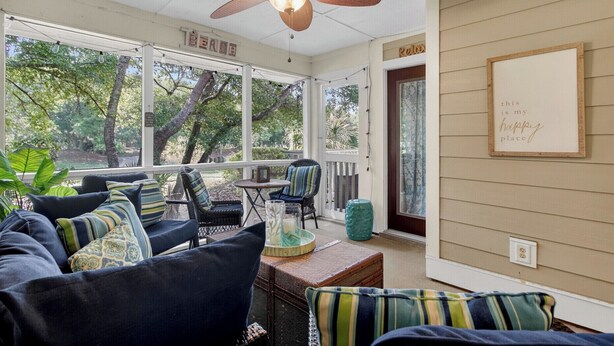 A covered porch with a ceiling fan, wicker furniture, and a view of trees.