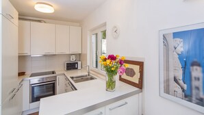Eine moderne Küche mit weißen Schränken, einer Mikrowelle, einem Backofen und einem Spülbecken. Auf der Arbeitsplatte steht eine Vase mit Blumen und an der Wand hängt ein gerahmtes Bild.
