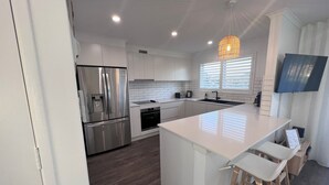 A modern kitchen with white cabinetry, stainless steel appliances, a large island with bar stools, and a TV mounted on the wall.