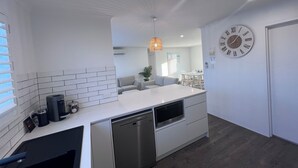 A modern kitchen with white cabinetry, a built-in dishwasher, and a dining area with a white table and chairs.