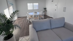 A modern living room with a grey sofa, a dining table with chairs, and a potted plant.