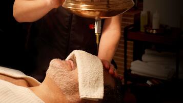 A person receiving a facial treatment with a metal basin and a towel covering their face.