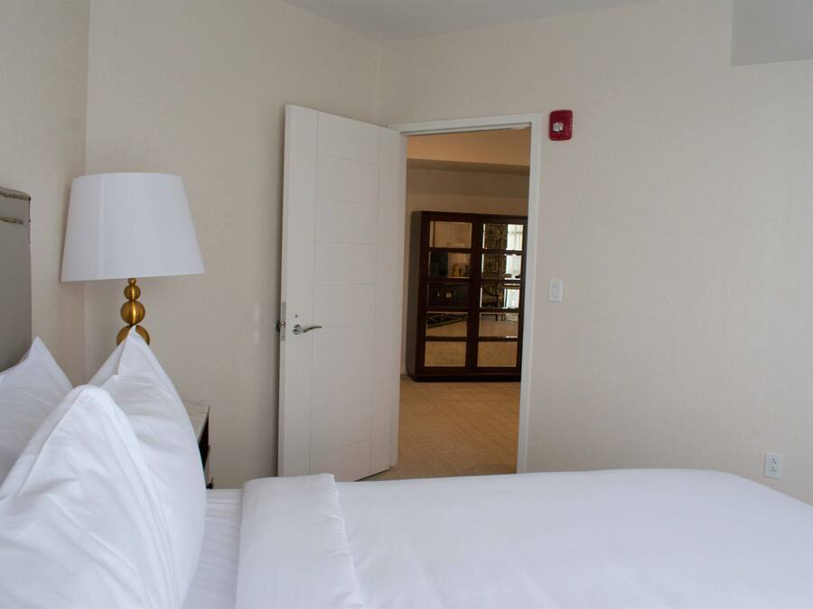 A hotel room with a bed, a lamp, and an open door leading to another room.