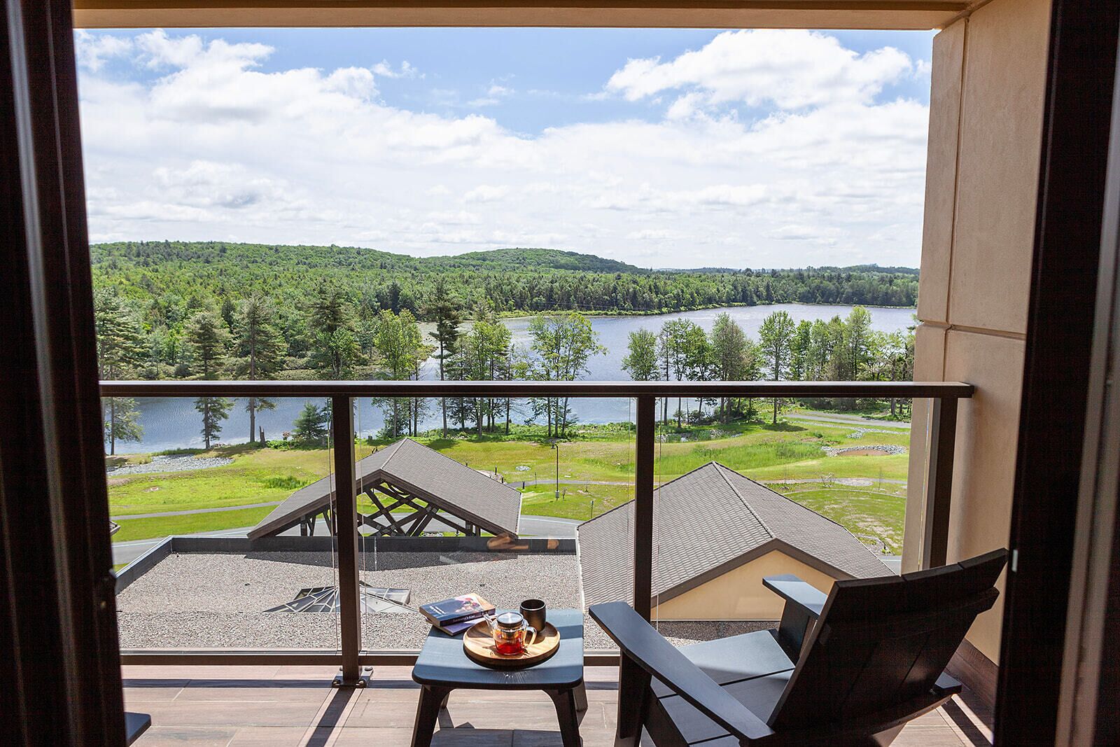 A balcony with a table and chairs, overlooking a lake and forested hills.
