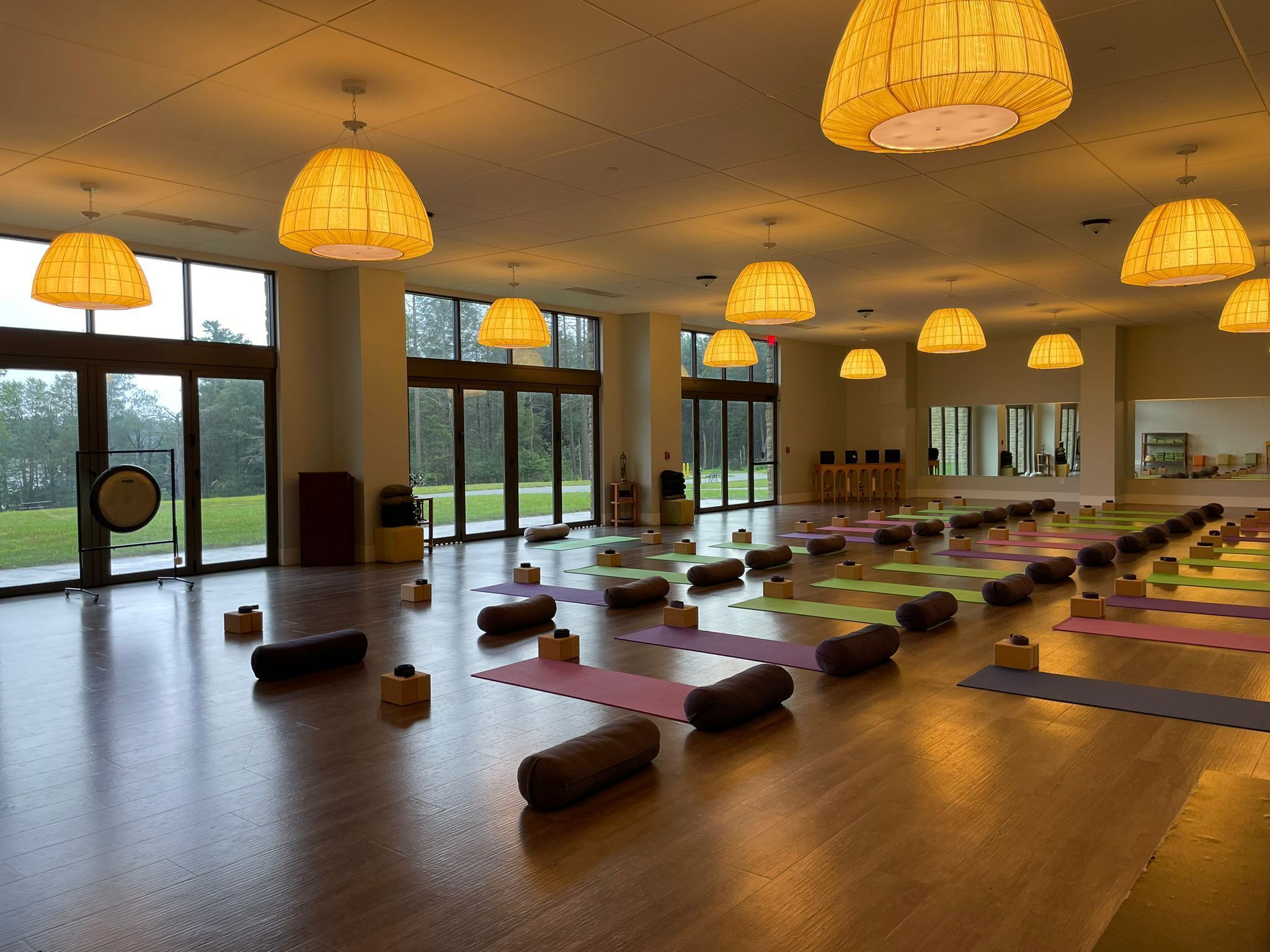 Amplia habitación con ventanas grandes, suelo de madera y varias esterillas de yoga dispuestas para actividades grupales.