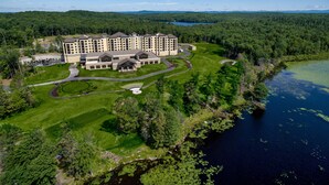 A large hotel with multiple buildings, a well-maintained lawn, and a lake nearby.