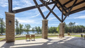 A covered patio area with stone pillars, wooden benches, and a view of a lake.