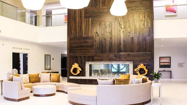 A modern lobby with a wooden accent wall, a seating area with sofas and ottomans, and a 'Museum Store' sign.