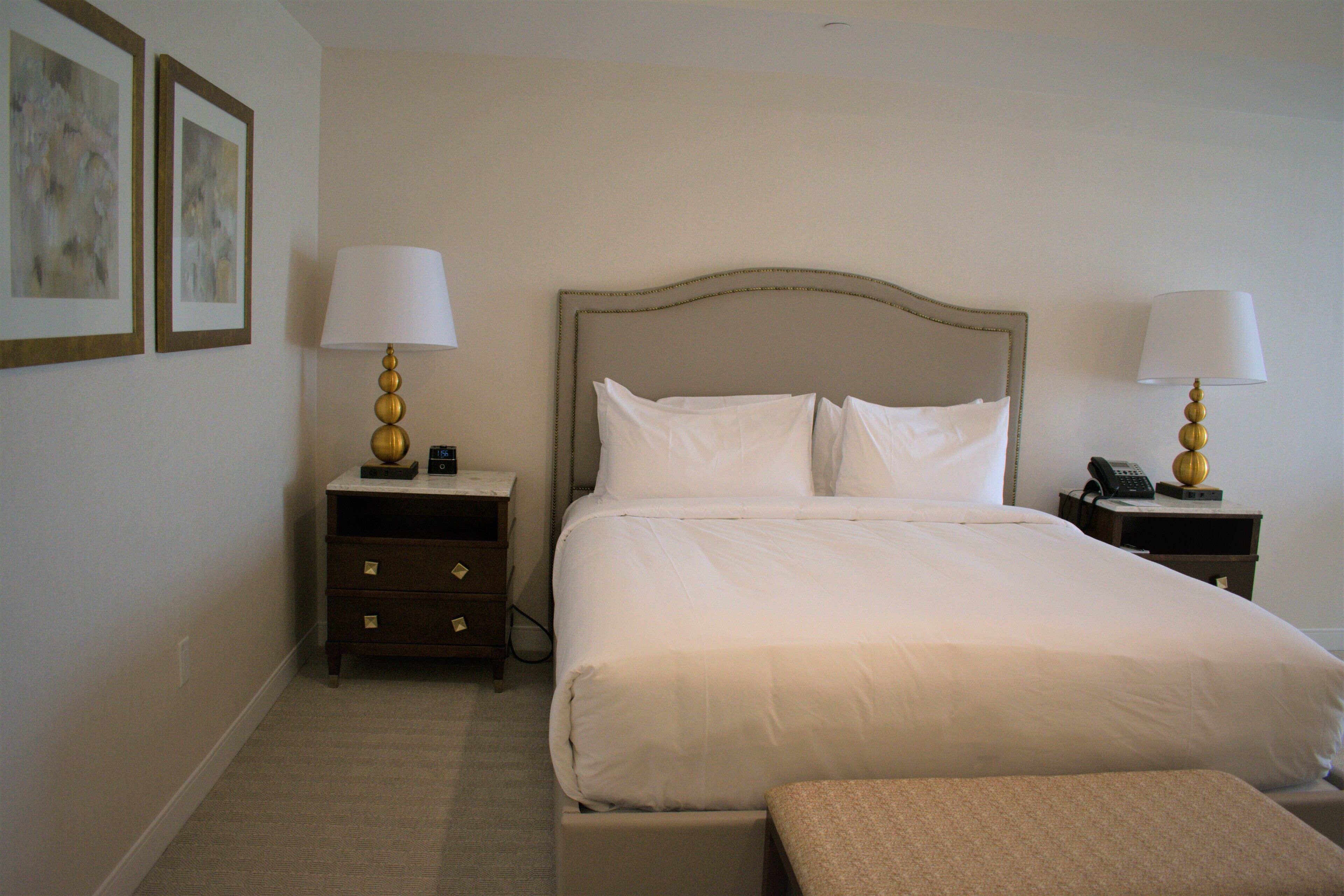 A hotel room with a large bed, two bedside tables, a nightstand, a bench, and two lamps.
