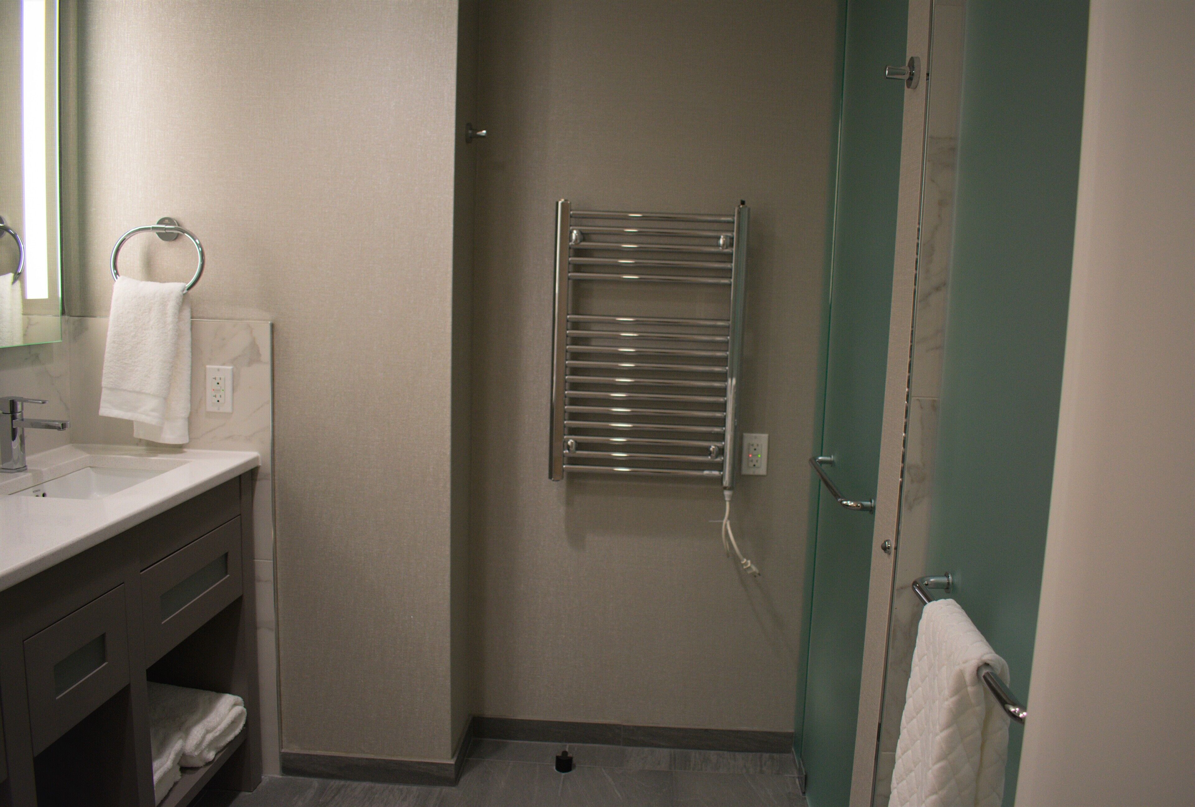 A bathroom with a sink, mirror, towel rack, and a towel hanging on the door.